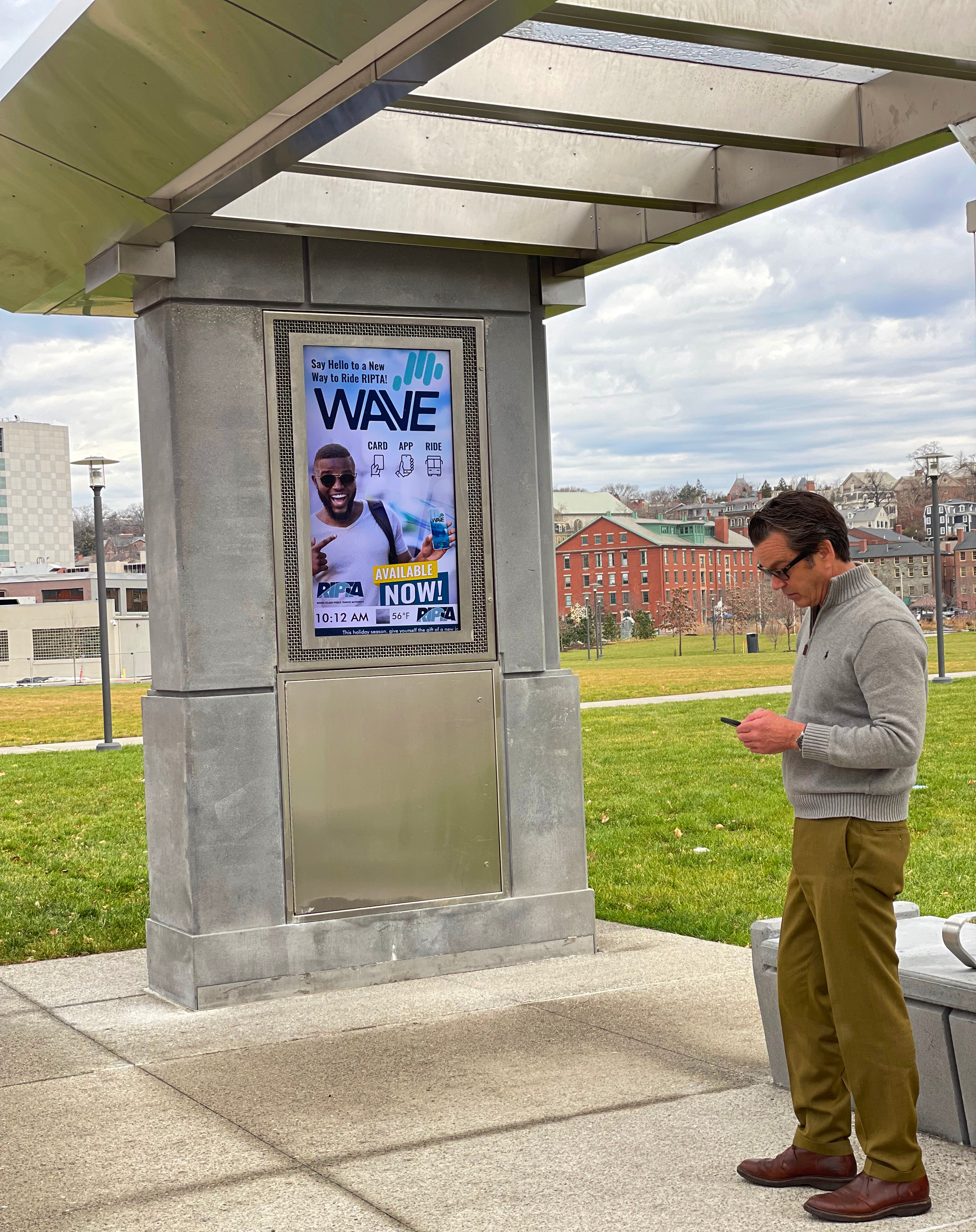 Rider waits at the Ship St. bus stop, the real-time information screen shows an advertisement for Wave.